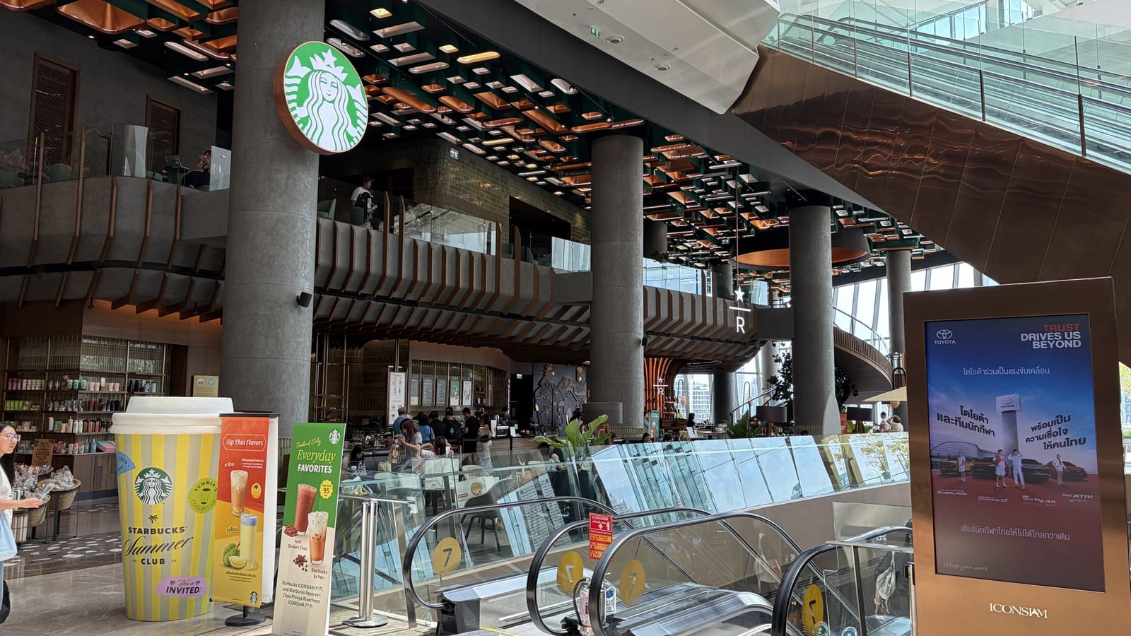 ICONSIAM 7階、エスカレーター脇から見た店舗入口。銅色と緑の天井装飾の下にスターバックスのロゴ看板が下がる