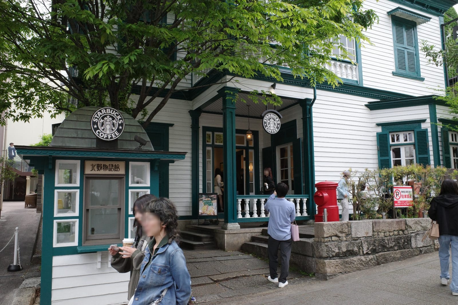 北野物語館の正面入口まわり。玄関ポーチ上の丸い「STARBUCKS COFFEE」サインを挟んで、左手に白いサインボックス、右手に赤い円筒形ポストが並ぶ