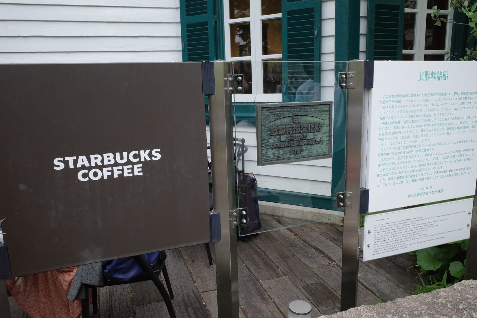 入口横の「STARBUCKS COFFEE」木製サインと、銅板の「登録有形文化財」プレート、白い「北野物語館」説明板