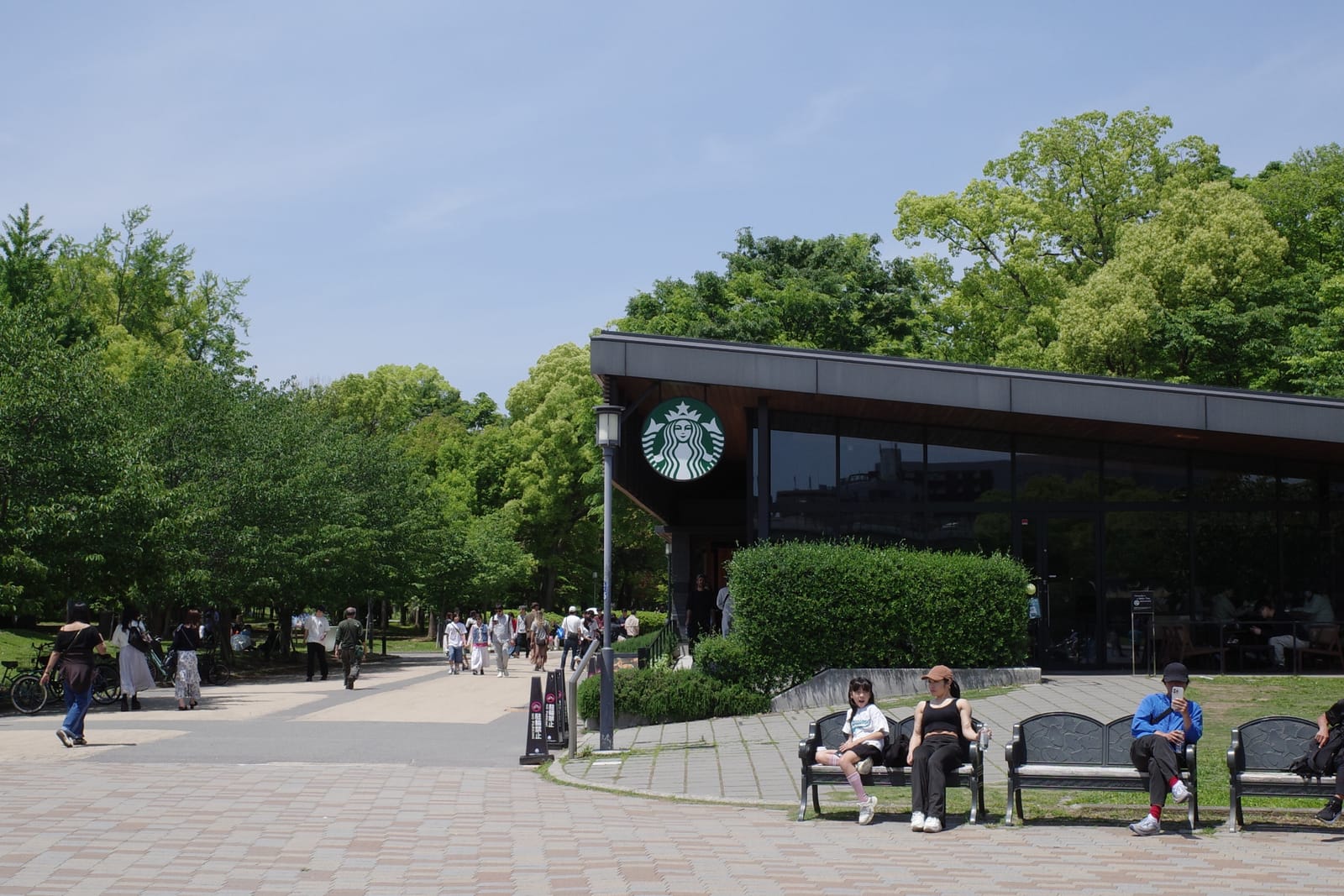 店舗外観のアップ。屋根の低い黒い木造店舗に大きな円形のスターバックスロゴ、店前のベンチに座って休む人々
